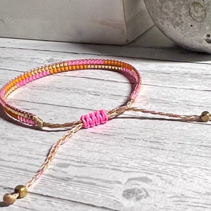 Peut inclure: Un bracelet en perles rose et or avec une fermeture r&eacute;glable nou&eacute;e. Le bracelet est fait de petites perles et a un design simple.