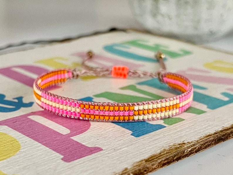 May include: A pink, orange, and white beaded bracelet with a brown cord closure.