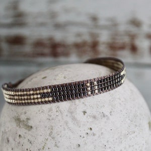 Könnte beinhalten: Ein braunes und weißes Armband mit geometrischem Muster.