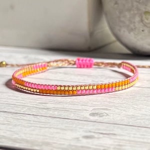 Peut inclure: Un bracelet en perles rose et orange avec un accent dor&eacute;. Le bracelet est fait de petites perles rondes et a un design simple et minimaliste.