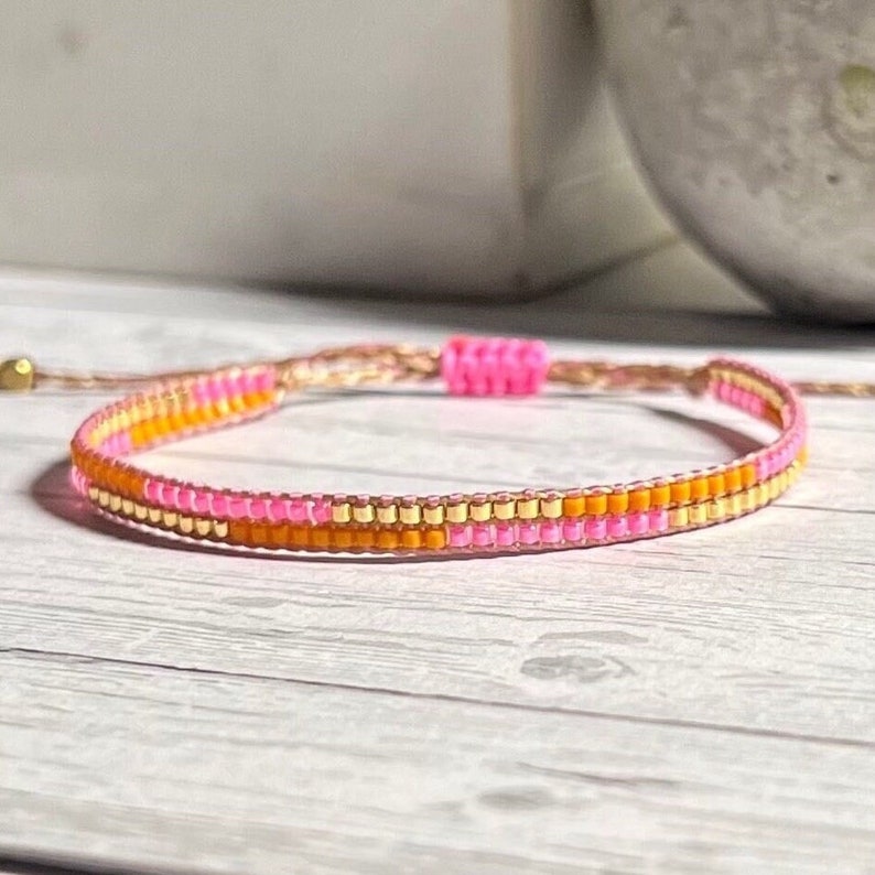 Peut inclure: Un bracelet en perles rose et orange avec un accent dor&eacute;. Le bracelet est fait de petites perles rondes et a un design simple et minimaliste.