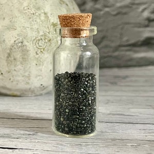 Peut inclure: Une petite bouteille en verre avec un bouchon en liège remplie de perles noires.