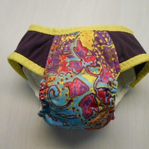 May include: A colorful patterned diaper cover with yellow trim and a dark purple fabric panel on each side.