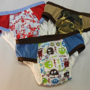 May include: Three pairs of underwear with different patterns. One pair is red and white with geometric shapes, another is camouflage, and the third is white with a colorful monster design.