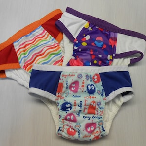 May include: Three pairs of reusable training underwear with different colorful patterns. One pair has a red and orange trim, another has a purple trim, and the third has a blue trim.
