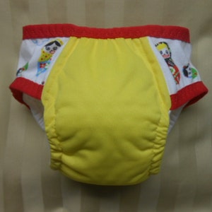 May include: Yellow training pants with red trim and a white print of dolls with colorful clothing.