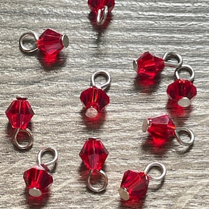May include: Ten red crystal beads with silver loops. Each bead has a faceted design and is attached to a silver loop.