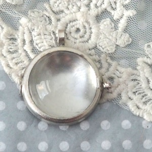 May include: A silver locket pendant with a clear glass insert. The locket is round and has a smooth, polished finish.