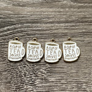 May include: Four gold-toned charms in the shape of a white teacup with the text "A CUP OF TEAD SOLVES EVERYTHING" in black. The charms have a gold-toned loop at the top for attaching to jewelry or other crafts.