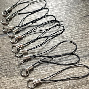 May include: A set of ten black string phone charms with silver metal rings. The charms are approximately 6 inches long.