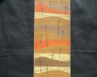 May include: A decorative textile panel featuring a landscape design with stylized hills in shades of brown, orange, and beige. Thin, black cross-like shapes are scattered across the hills. The panel is set against a black background.