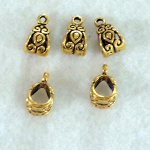 May include: Five gold-colored metal jewelry findings. Three are bell-shaped with ornate designs, and two are open-ended with a ribbed texture. All have small loops for attaching to other components.