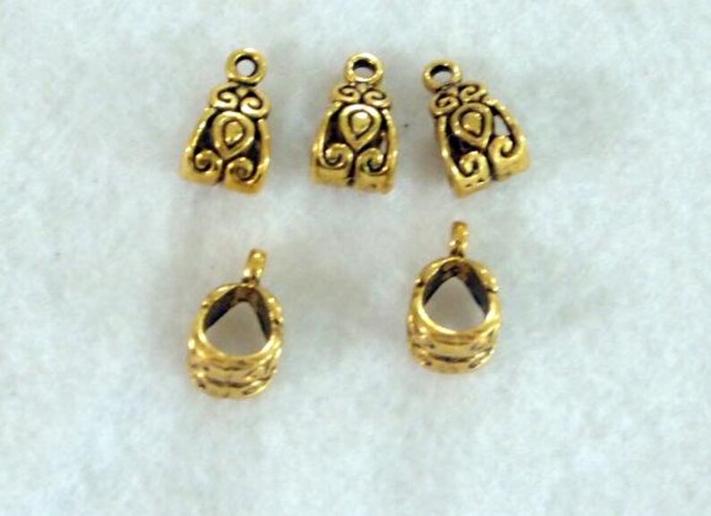 May include: Five gold-colored metal jewelry findings. Three are bell-shaped with ornate designs, and two are open-ended with a ribbed texture. All have small loops for attaching to other components.