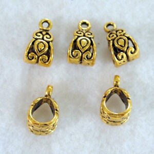 May include: Five gold-colored jewelry findings. Three are bell-shaped with decorative swirls and a loop at the top. The other two are open-backed with a textured pattern and a loop.