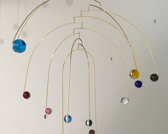 May include: A brass mobile with multiple hanging spheres in various colours, including blue, red, green, yellow, and clear. The spheres are suspended from a series of curved brass arms.