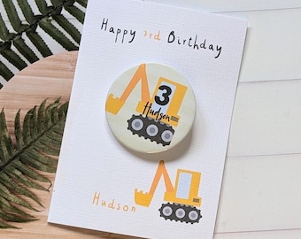 May include: A yellow and white birthday card with a yellow excavator design. The card says "Happy 3rd Birthday" and "Hudson".