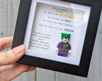 May include: A framed artwork featuring a Lego Joker figure. The black frame surrounds a white background with text that reads, "as smart as Iron Man, as strong as Hulk, as brave as Batman, and as cool as the Joker."