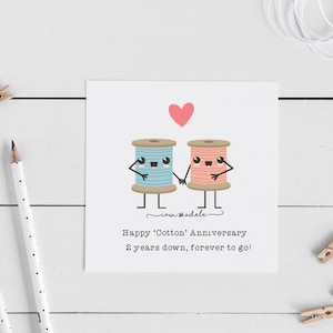 May include: A greeting card with a pink heart and two cartoon spools of thread, one blue and one pink, holding hands. The text reads "Happy 'Cotton' Anniversary 2 years down, forever to go!"