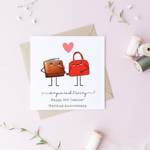May include: A white card with a brown wallet and a red handbag holding hands. The card says "Wayne and Tracey Happy 3rd 'Leather' Wedding Anniversary".