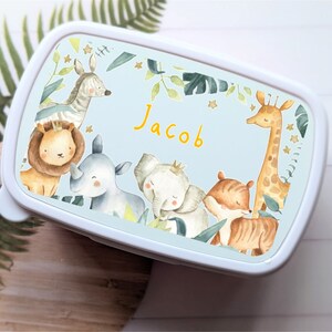 May include: A blue lunchbox with a white border and a jungle animal theme. The lunchbox features a lion, zebra, rhino, elephant, tiger, and giraffe. The name "Jacob" is written in yellow letters on the front of the lunchbox.