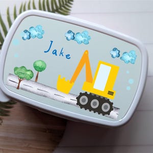 May include: A blue lunchbox featuring a yellow excavator design. The excavator has a yellow cab and black wheels. The lunchbox is personalised with the name "Jake".