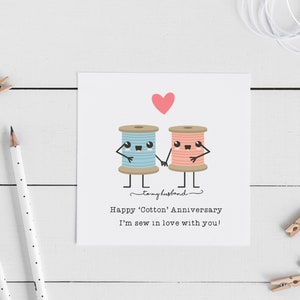 May include: A greeting card with a pink heart and two cartoon spools of thread, one blue and one pink, holding hands. The text reads "Happy 'Cotton' Anniversary! I'm sew in love with you!"