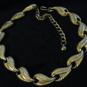 May include: A vintage gold-tone necklace featuring a leaf design. The necklace has a series of textured, stylized leaf-shaped links with a two-tone finish. The adjustable chain allows for a customized fit. The necklace is a classic piece of jewelry.