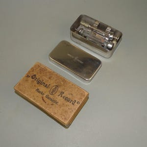 Pequeña caja metálica/caja de cartón alemana vintage con jeringa de vidrio de 2 ml. Disco original.