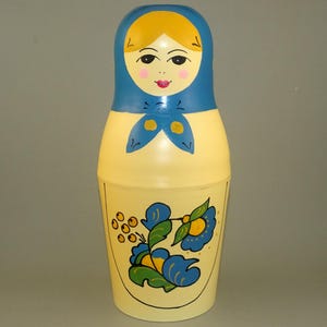 Könnte beinhalten: Eine traditionelle russische Nistpuppe, auch bekannt als Matrjoschka-Puppe, mit einem gelben und blauen bemalten Design. Die Puppe ist mit einem Blumenmuster und einem Frauen Gesicht bemalt.