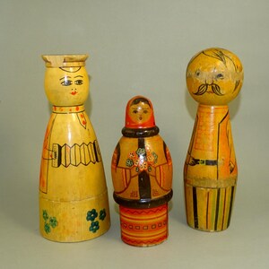Puede incluir: Tres muñecas de madera con caras y ropa pintadas. Las muñecas están pintadas en amarillo, rojo, naranja, negro y verde. Las muñecas son muñecas rusas tradicionales.