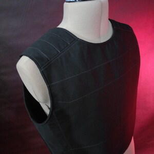 May include: Black tactical vest with a quilted design. The vest has a high neckline and a sleeveless design.