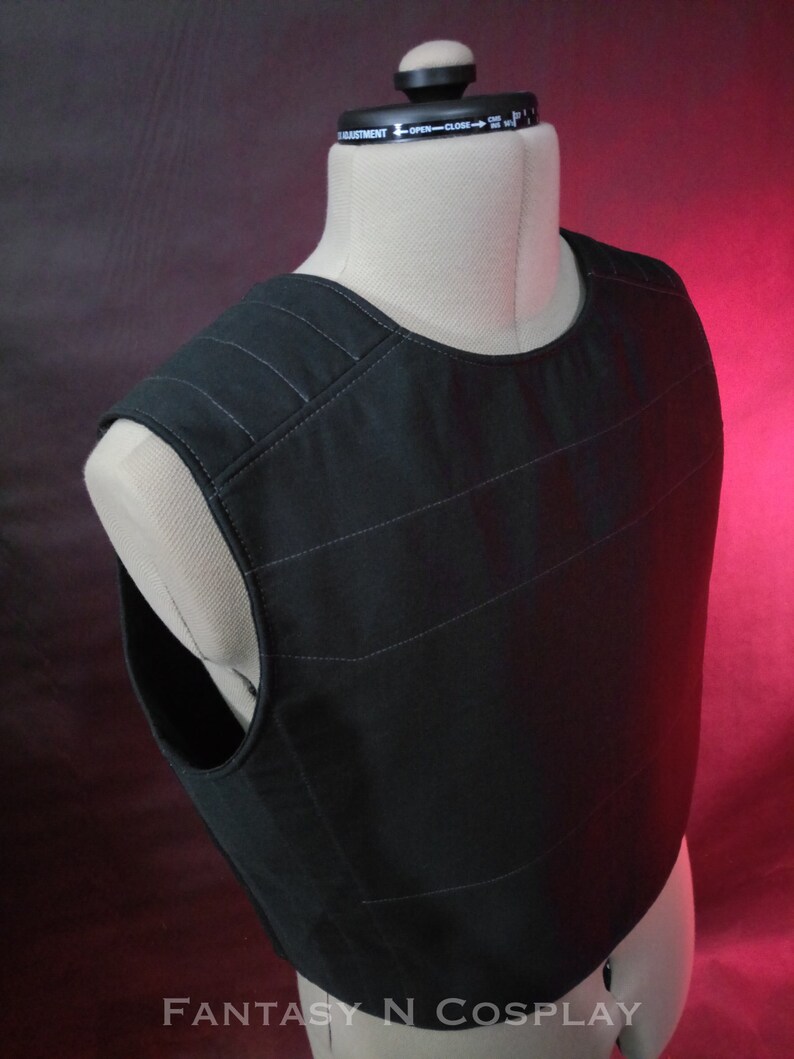 May include: Black tactical vest with a quilted design. The vest has a high neckline and a sleeveless design.
