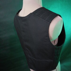 May include: Black sleeveless vest with a zipper closure and multiple pockets. The vest has a textured fabric and is made of a durable material.