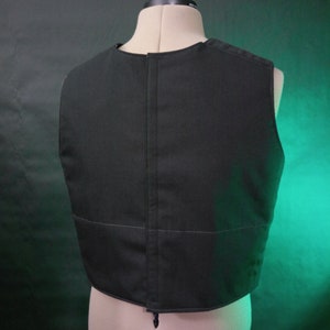May include: Black sleeveless vest with a zipper closure in the back. The vest is made of a thick, durable fabric and has a simple, classic design.