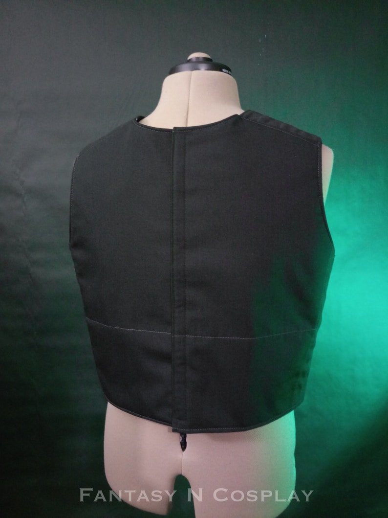 May include: Black sleeveless vest with a zipper closure in the back. The vest is made of a thick, durable fabric and has a simple, classic design.