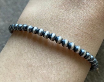 May include: A silver bracelet with black and white beads. The bracelet is made of small, round beads that are strung together in a simple design.