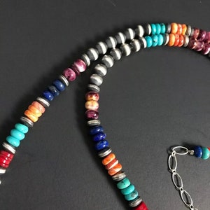 May include: A multi-colored beaded necklace with a silver chain clasp. The beads are made of turquoise, lapis lazuli, coral, and other stones. The necklace is a beautiful example of Native American jewelry.