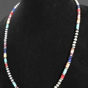 May include: A multi-colored beaded necklace with silver beads. The beads are in a repeating pattern of turquoise, orange, red, purple, blue, and silver.