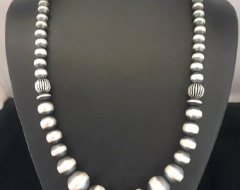 May include: A silver necklace with round beads and a decorative bead at each end. The necklace is displayed on a black mannequin.