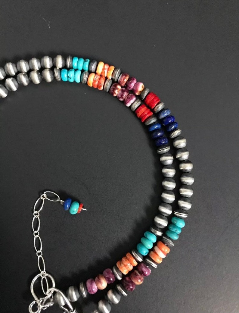 May include: A multi-strand necklace with silver beads and colorful stones. The stones are arranged in a rainbow pattern, starting with purple, then orange, turquoise, blue, and ending with lapis lazuli.