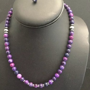 May include: A purple and silver beaded necklace with a silver clasp. The beads are round and have a marbled pattern.