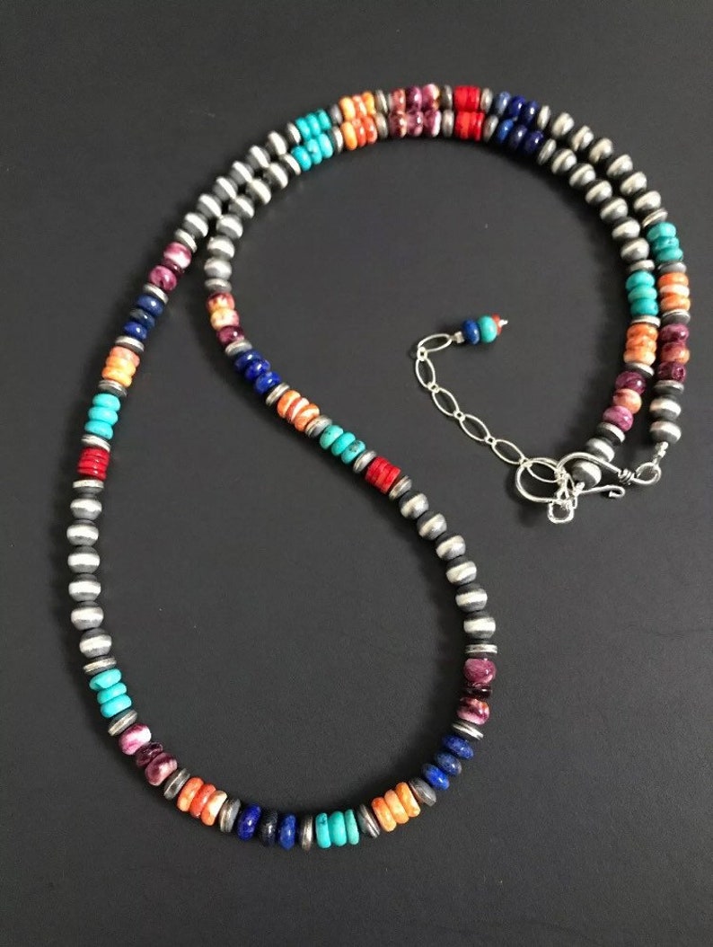 May include: A multi-colored beaded necklace with silver accents. The necklace features turquoise, coral, lapis lazuli, and other stones.