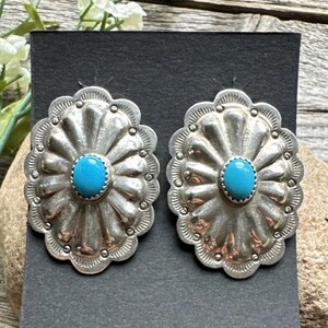 May include: A pair of silver earrings with a turquoise stone in the centre of each earring. The earrings are shaped like a flower with a scalloped edge.