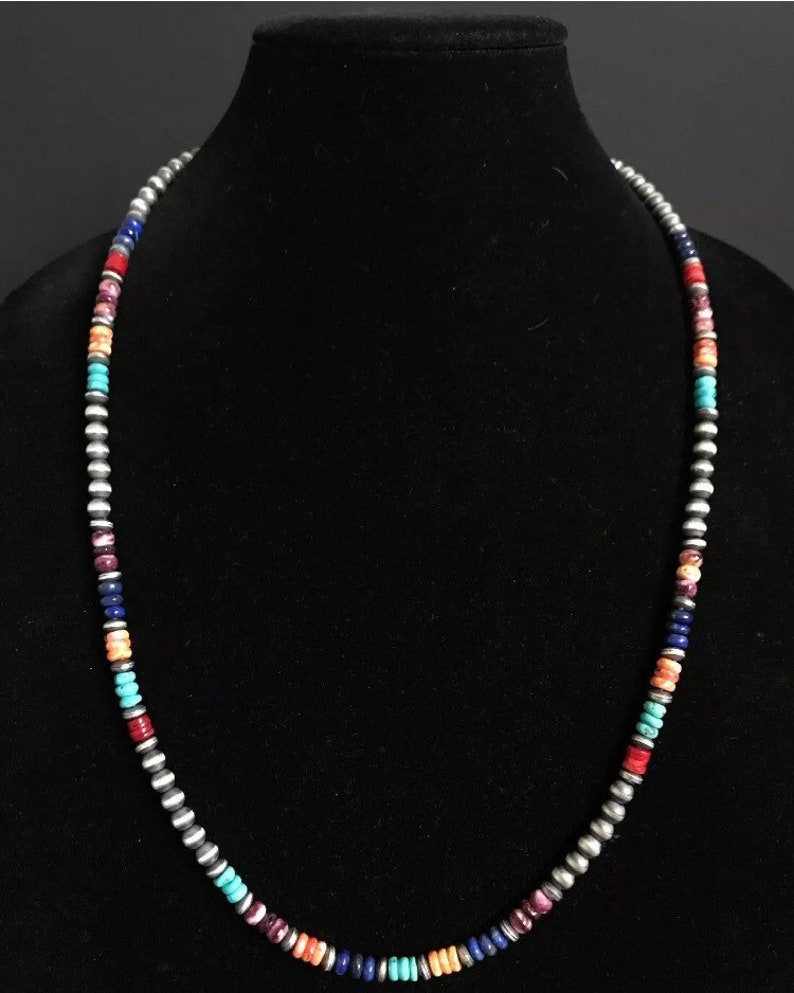 May include: A multi-colored beaded necklace with silver beads. The necklace features turquoise, lapis lazuli, coral, and other stones.