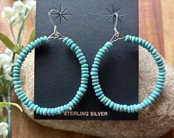 May include: Turquoise beaded hoop earrings with sterling silver findings. The earrings are displayed on a black card with the text "STERLING SILVER". The hoops are made of small, round, light blue beads.