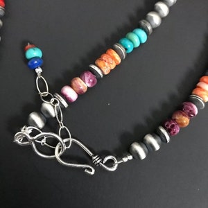 May include: A multi-colored beaded necklace with a silver clasp. The beads are made of turquoise, coral, and other stones. The necklace is a beautiful example of Native American jewelry.