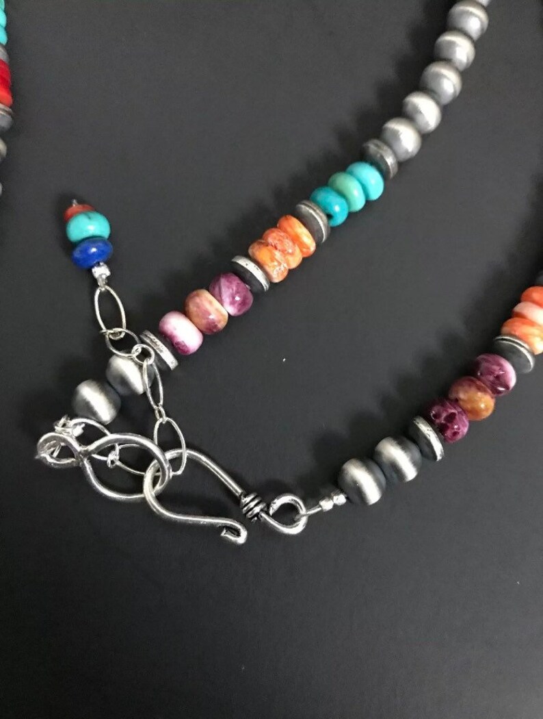 May include: A multi-colored beaded necklace with a silver clasp. The beads are made of turquoise, coral, and other stones. The necklace is a beautiful example of Native American jewelry.