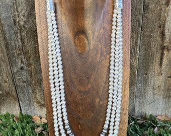 May include: A three-strand pearl necklace with silver beads and silver accents. The necklace is displayed on a wooden stand.