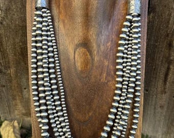May include: A silver multi-strand necklace with a silver bead design. The necklace has a silver clasp and is displayed on a wooden mannequin.