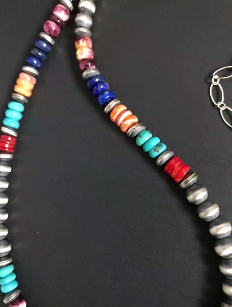 May include: A multi-colored beaded necklace with silver beads. The beads are in a rainbow pattern, with red, orange, yellow, green, blue, and purple beads.